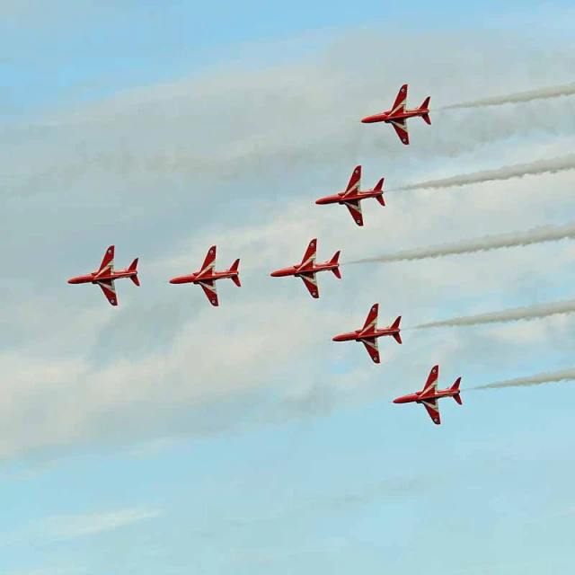 seven red jets are flying in formation with smoke trailing behind them