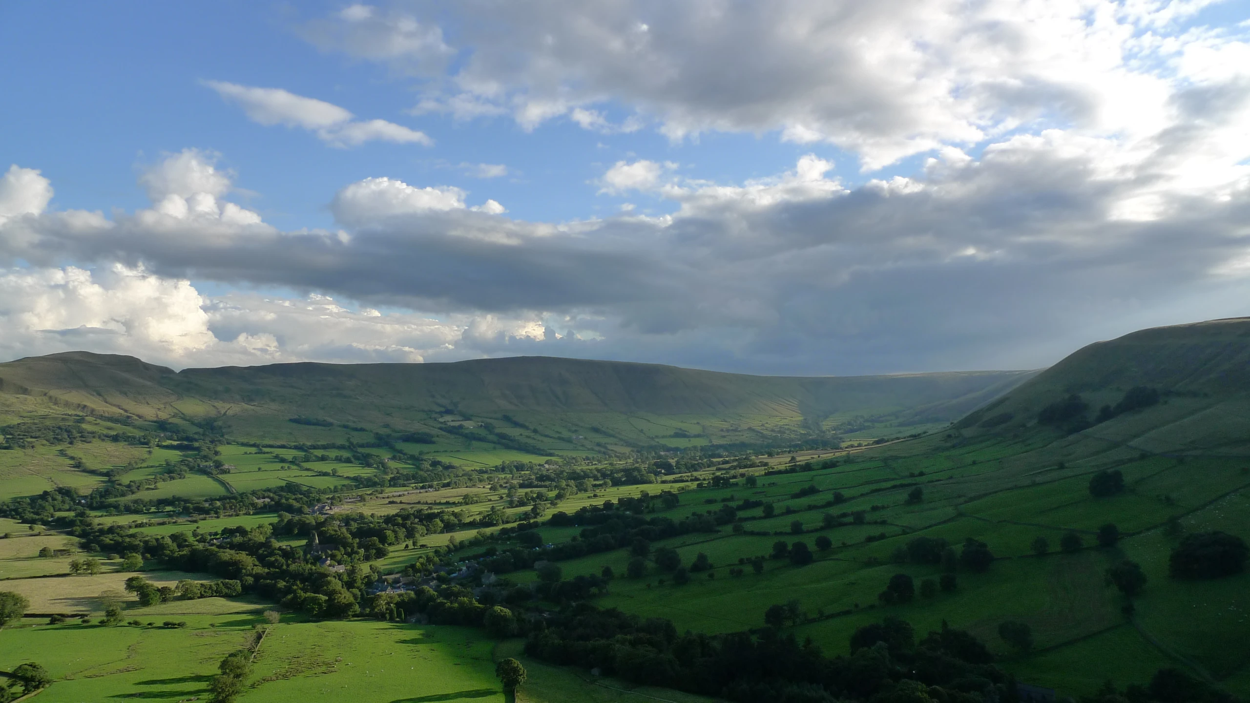 green valley with rolling hills and trees under a blue cloudy sky