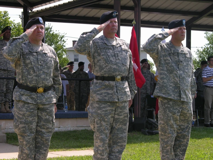 three soldiers are saluting while a crowd looks on