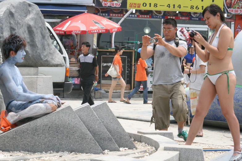 two women taking pictures of an asian man in the street