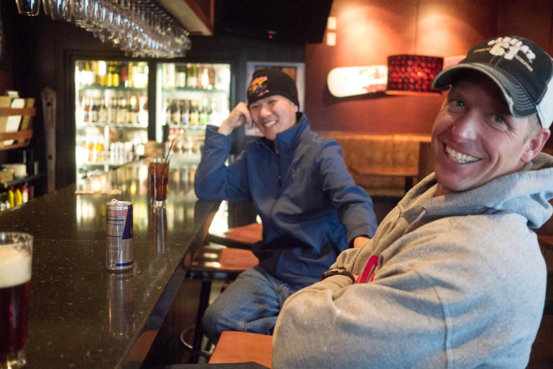 two people sitting at a bar with beer