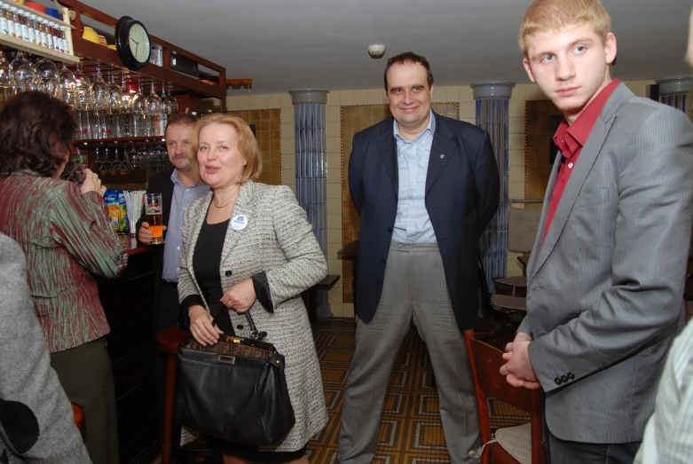 two men and one woman are standing next to each other with a man in the background wearing suit and tie holding a briefcase