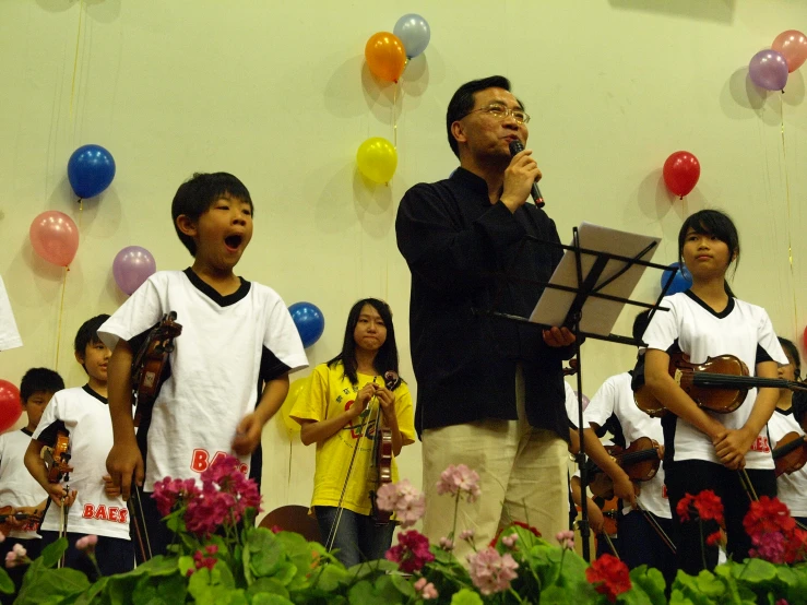 a man singing with a musical instrument in front of a group of children