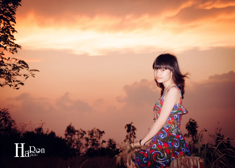 a pretty young lady standing in a field next to trees