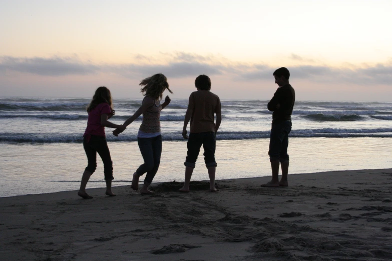 five people stand on the beach at sunset