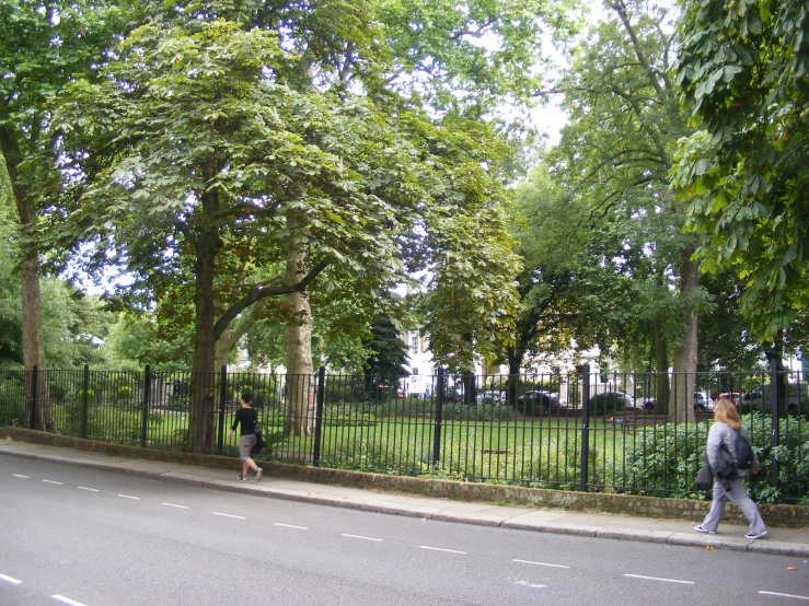 a large black gate is across the street from two people walking