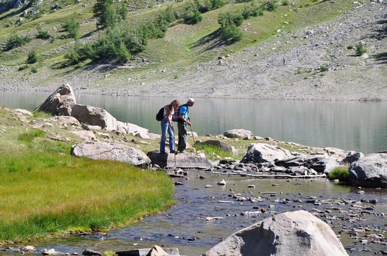 two hikers are walking along the river bank