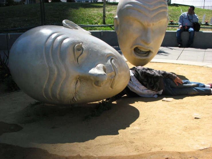 a woman sitting on the ground next to a statue of a person
