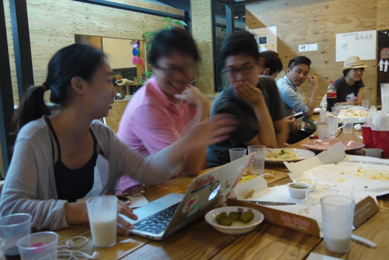 four people are eating together with laptops and papers on the table