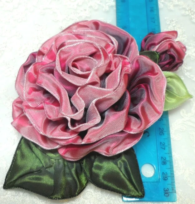 a pink rose and green leaves brooch resting on a piece of fabric