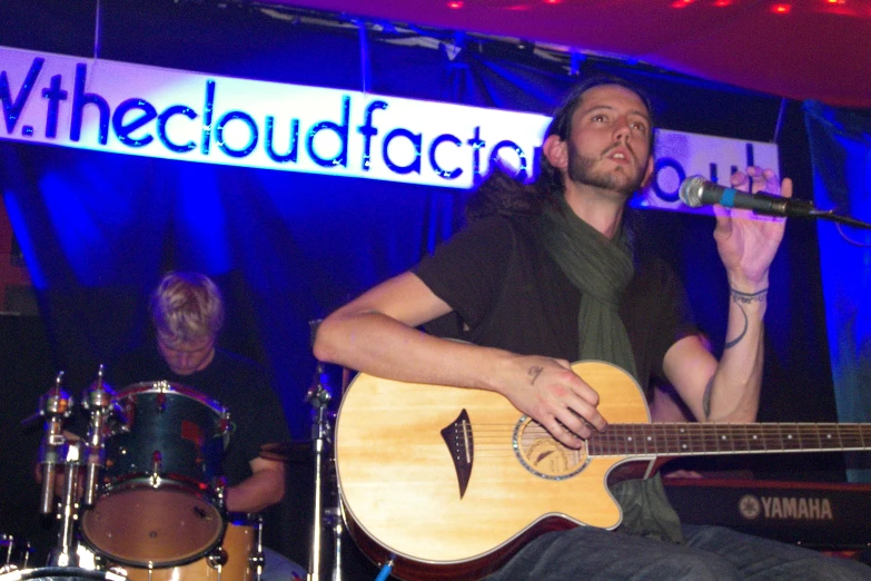 a person sitting on a stage playing a guitar and another male singing into a microphone