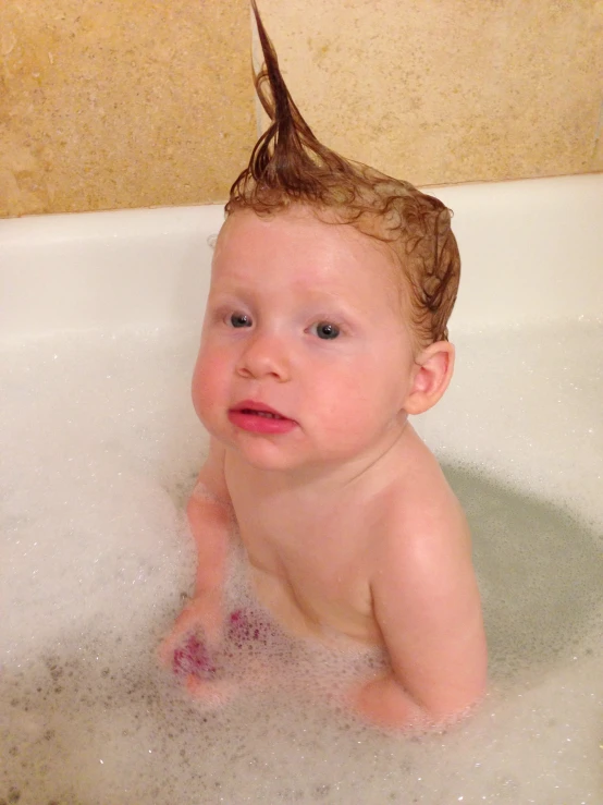 a toddler in a bathtub wearing a hairbrush on his head