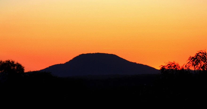 a silhouetted mountain and tree is at the background