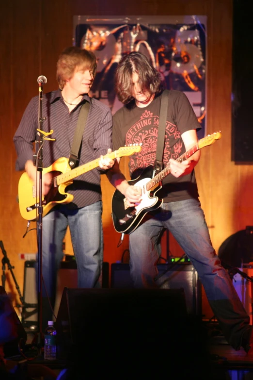 two people that are standing near one another playing the guitar