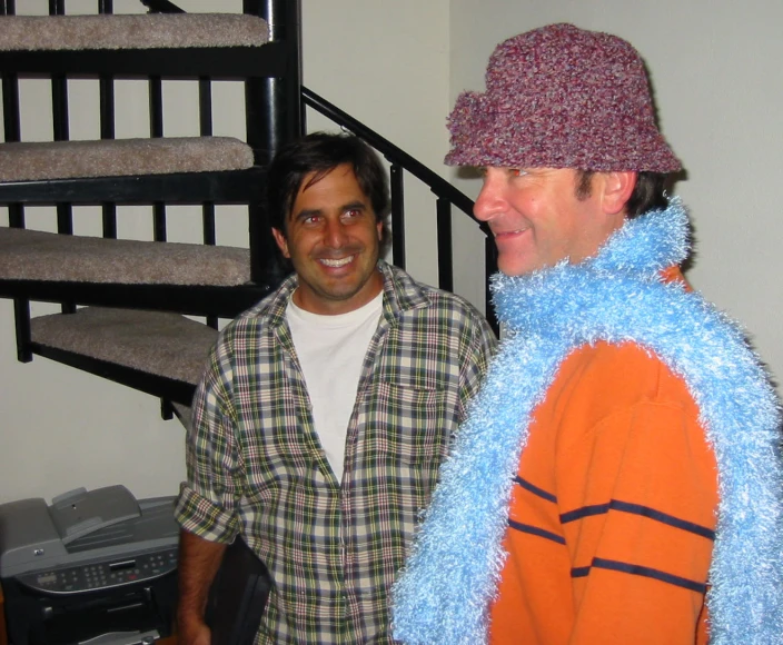 two men smile as they stand together near an spiral staircase