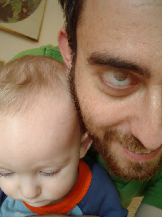 a bearded man holds his young child in one arm