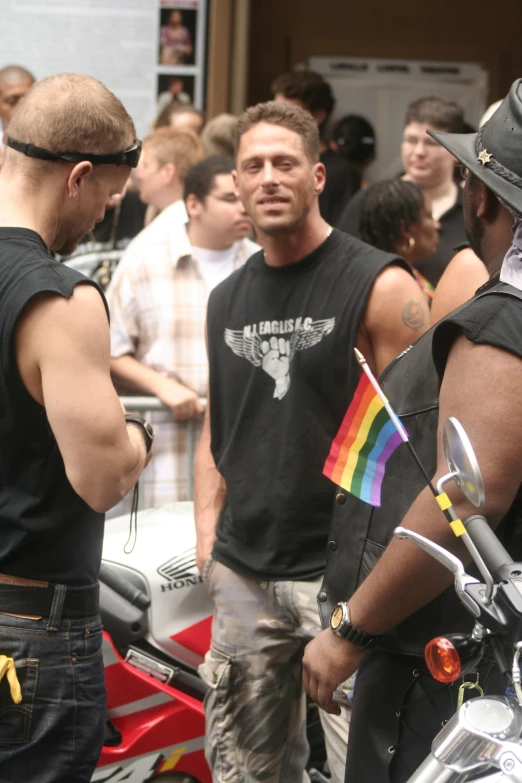 three men standing together with some bikes and people in background