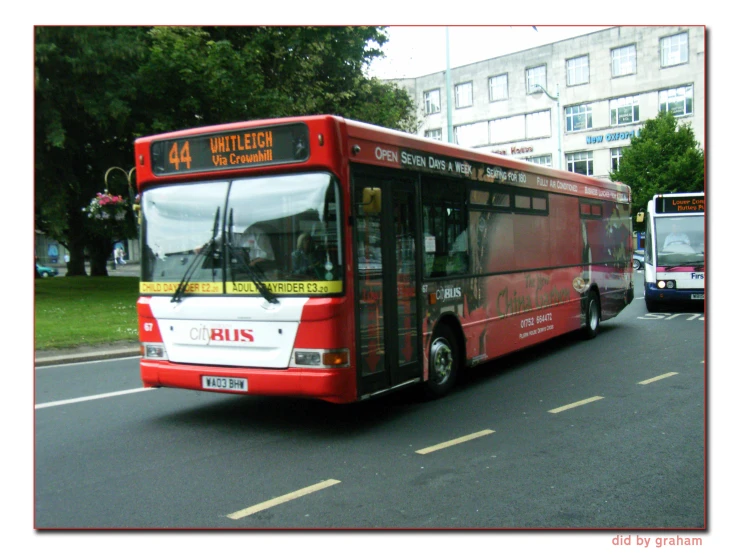 a red bus driving on the street, with another bus behind it