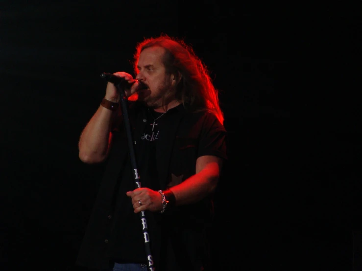 a man with long hair and wearing blue jeans holds a microphone in front of him while singing into the microphone