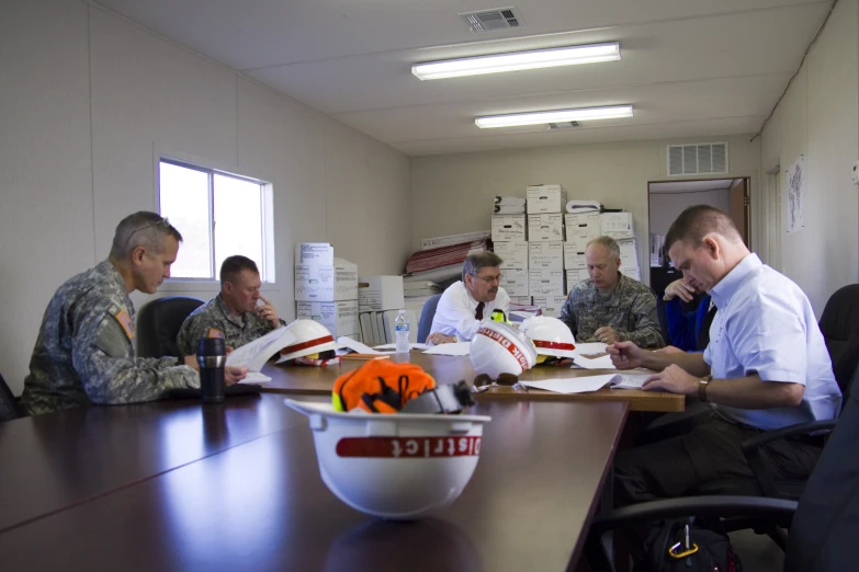 five men are sitting at a long table working on some paperwork