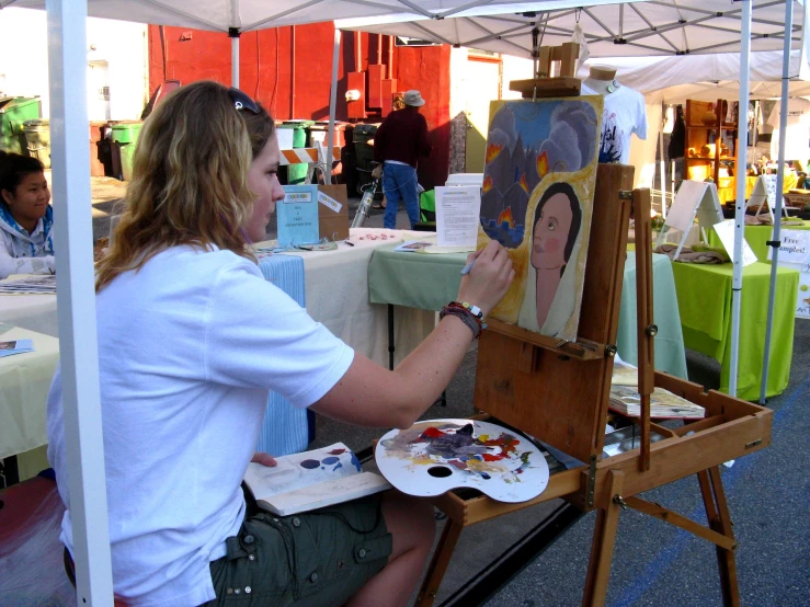 a woman painting an image on a canvas at an outdoor event