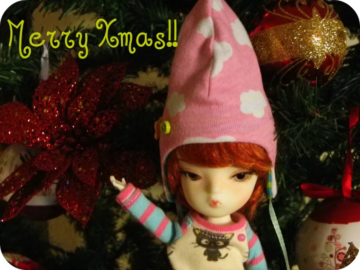 a cute little doll wearing a pink hat next to a christmas tree