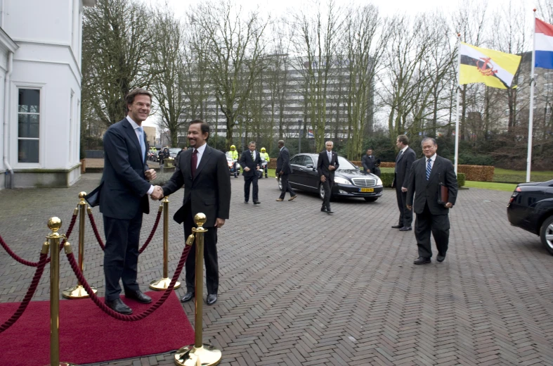 two men shaking hands over a red carpet