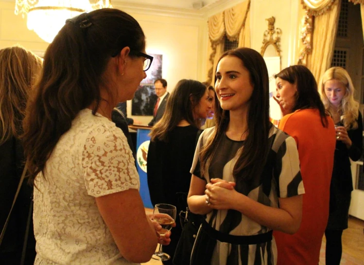 two women are standing together talking while holding glasses