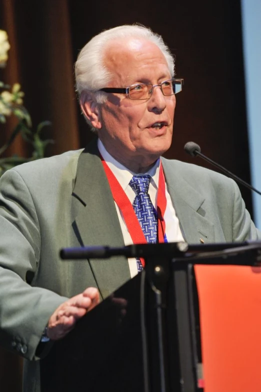 an older man in suit and tie speaking on stage