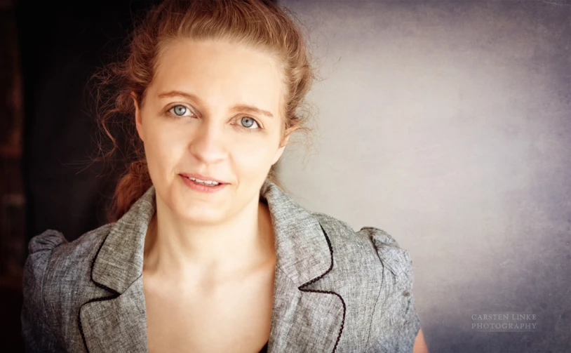 a woman in gray suit standing in front of a wall