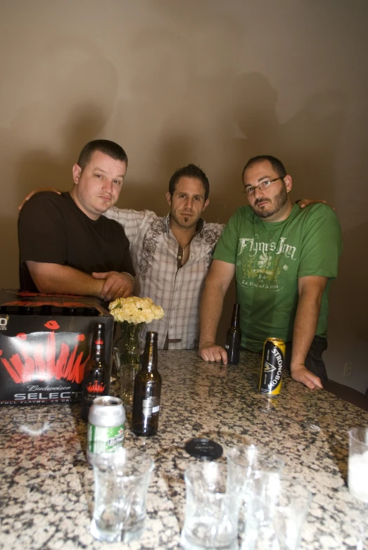 three men pose for a picture while sitting at a table full of bottles and glasses