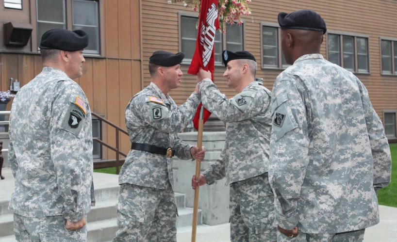 five men in camouflage uniforms hold up the flag