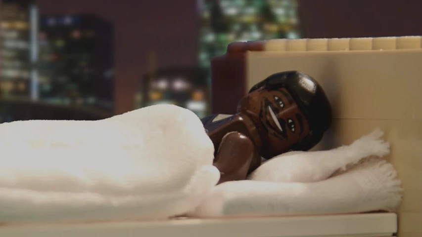 a plastic doll is lying in a bed with blankets