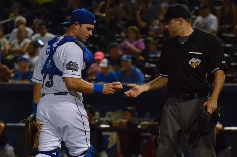 two baseball players talking while one is handing another a bat