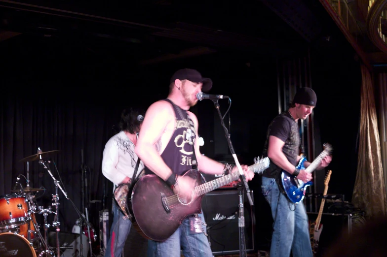 three men are singing into the microphone with guitar