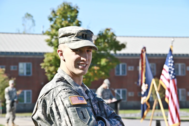 a smiling man in military uniform standing next to three flags