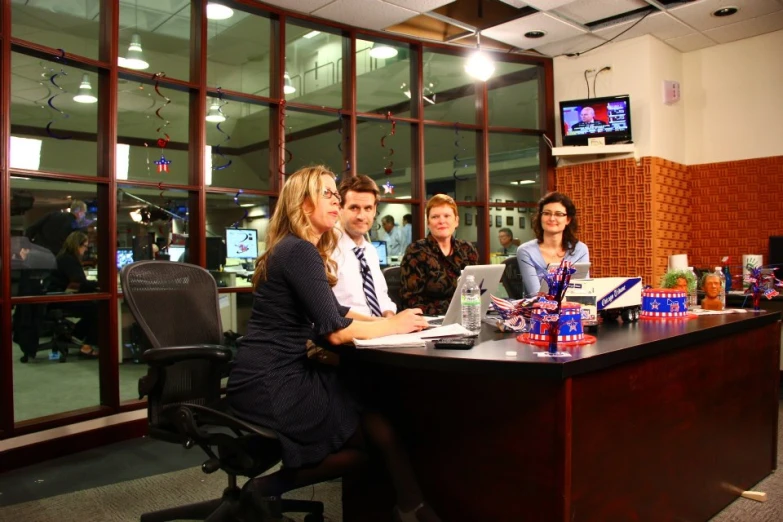 five people sitting at a desk with a laptop computer in a conference room