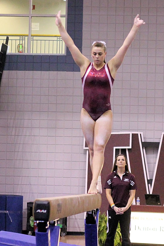 a woman standing on top of a wooden beam while wearing a maroon swimsuit