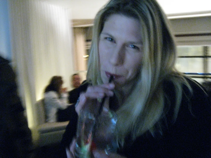 a blonde woman blowing on the water in a glass bottle