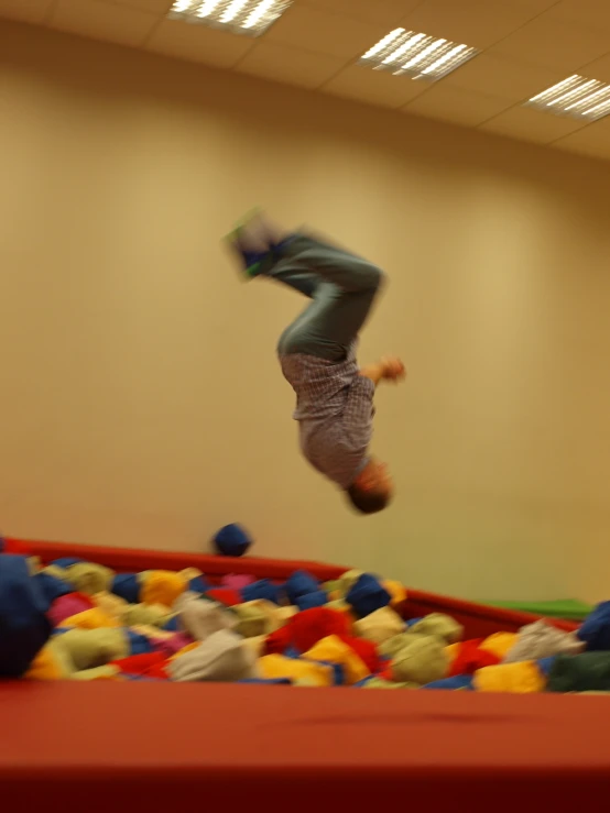 person in blue shorts doing tricks over a plastic ball pit