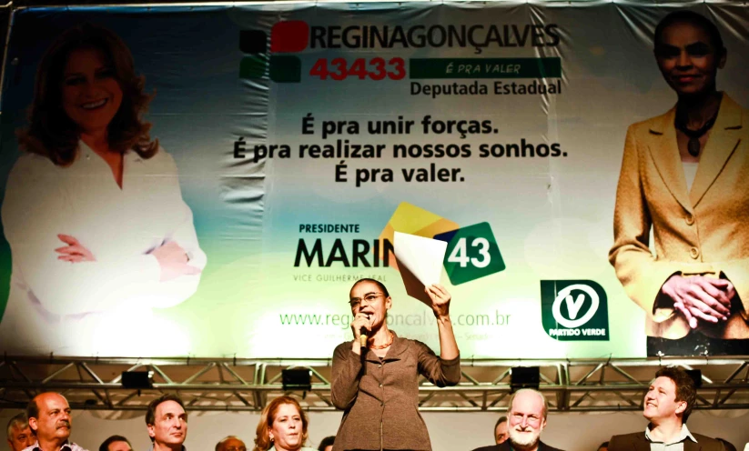 woman holding a paper while singing into a microphone with others watching