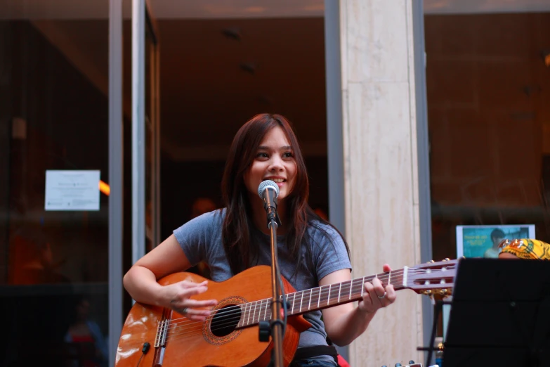 a woman singing and playing the guitar with an outdoor background