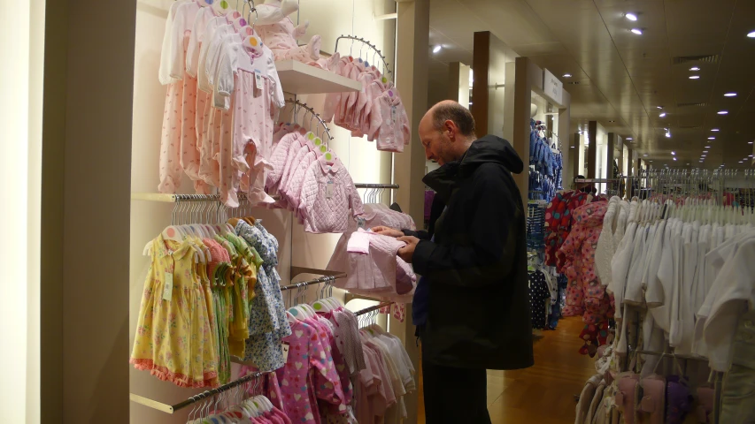 a man looking at some baby clothes on a rack