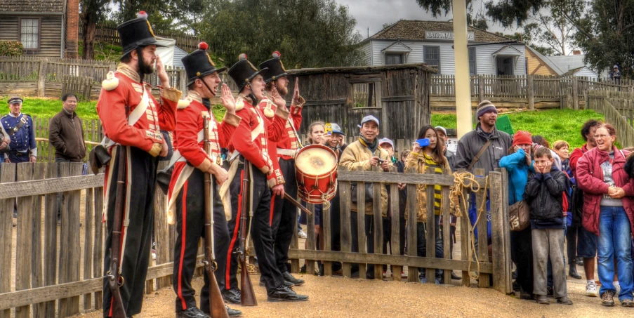 people at a wooden gate watching men in uniforms perform