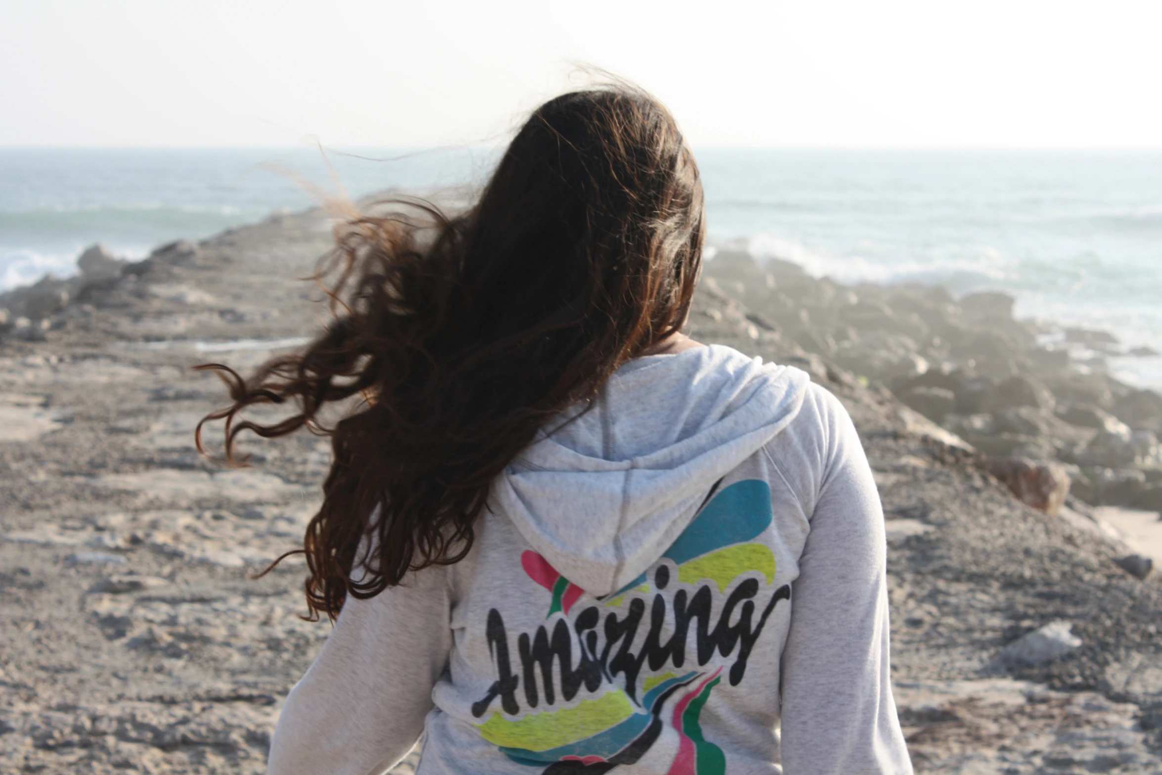 the girl is walking near the rocky shoreline