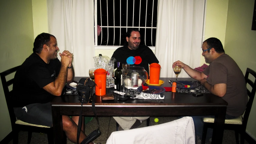 three men sitting at a table eating while holding drinks