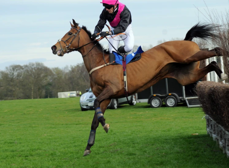 a jockey riding on the back of a horse while jumping over a jump