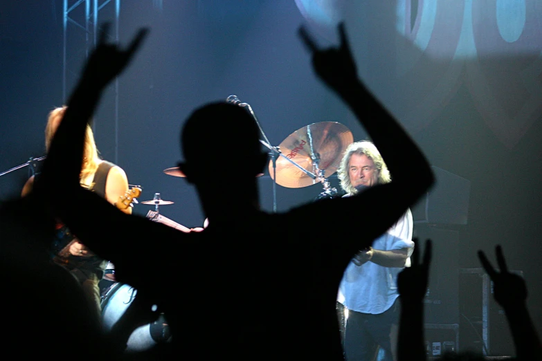 someone at a concert with their arm raised in the air and two guitar players behind them