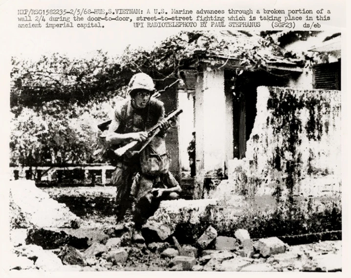 a man in white hat carrying a rifle next to wall