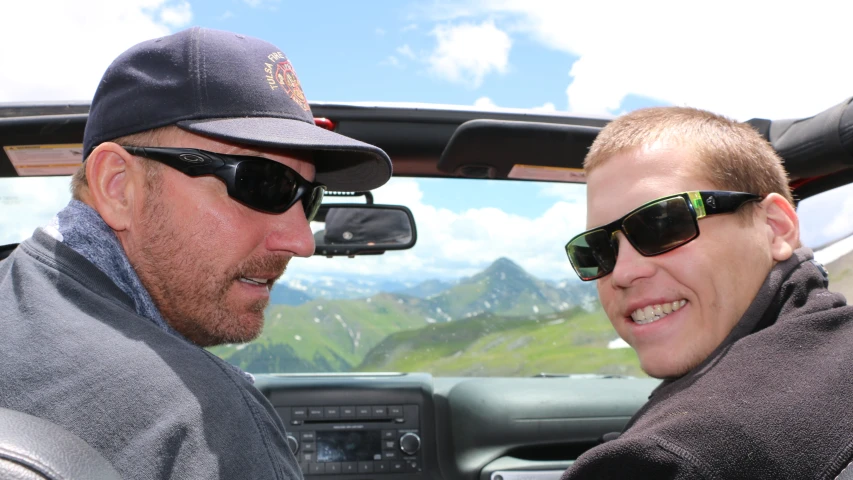 two men in sunglasses sit in the drivers seat of a truck